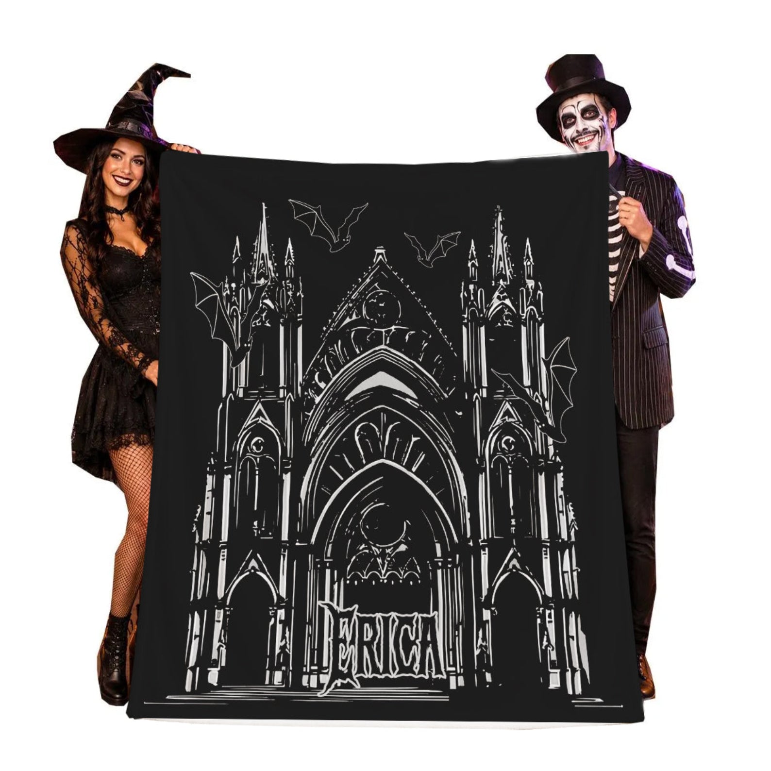 A large black Halloween-themed blanket featuring a white line art illustration of a gothic cathedral and bats, held up by two people in costume against a plain white background.