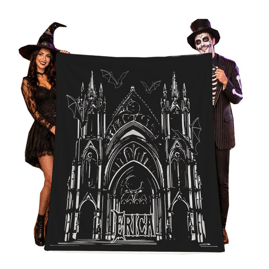 A large black Halloween-themed blanket featuring a white line art illustration of a gothic cathedral and bats, held up by two people in costume against a plain white background.